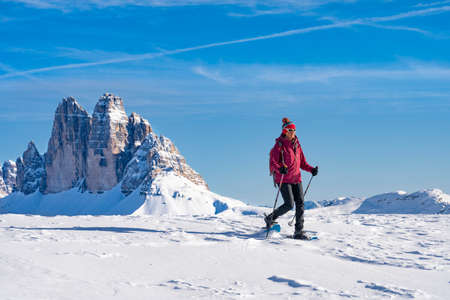 active senior woman snowshoeing under the famous Three Peaks from Prato Piazzo up to the Monte Specie in the three oeaks Dolomites area near village of Innichen, South Tyrol, Italyの写真素材