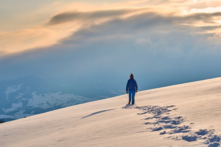 Hiker on top of a snowy mountain in the rays of the setting sunの写真素材