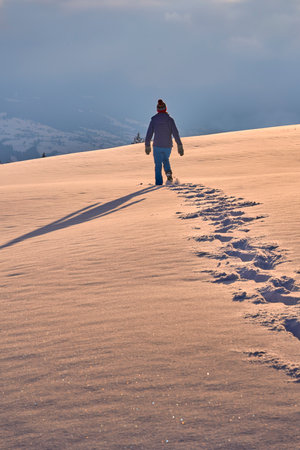 Hiker walking on snow dune at sunset in winter mountains.の写真素材