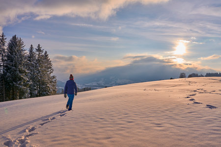 Man walking on snow in winter mountains at sunset. Beautiful winter landscape.の写真素材