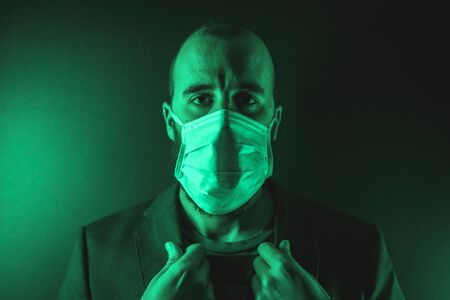 Gaze of a young Caucasian man with a scarf in the coronavirus pandemic with a green background, Covid-19の写真素材