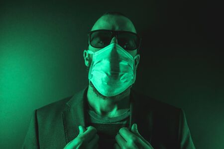 A young Caucasian man with a scarf and sunglasses in the coronavirus pandemic with a green background, Covid-19の写真素材