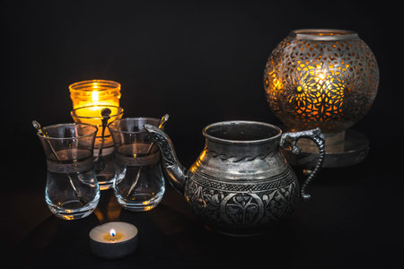 Metal cup and three Turkish glasses on a black background lit by candles