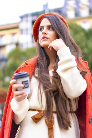 Street style, portrait of a caucasian woman dressed in red and with a skirt sitting in the city having a coffeeの写真素材