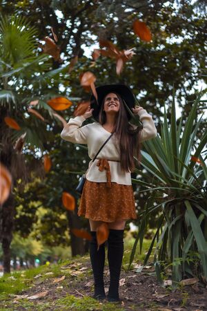 A young brunette with a street look at a photo shoot in autumn with tree leaves fallingの写真素材
