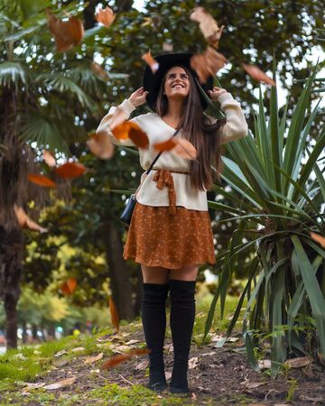 A young smiling brunette with a street look at an autumn photo shoot with falling tree leavesの写真素材