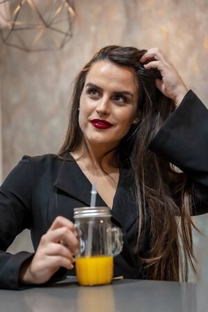 A young caucasian brunette in a coffee shop drinking orange juice, street styleの写真素材