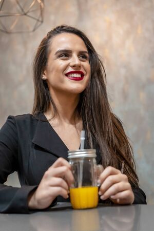 A young caucasian brunette smiling in a coffee shop drinking orange juice, street styleの写真素材