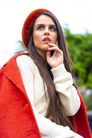 Street style, a young caucasian brunette dressed in red and wearing a red hat sitting in a city parkの写真素材
