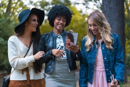 Lifestyle session. Three good friends in a park, a blonde, a brunette and a Latin girl with afro hairの写真素材