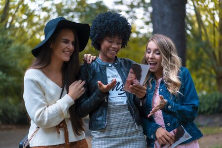 Lifestyle session. Three young friends hallucinating with a park flyer, a blonde, a brunette and a Latin girl with afro hairの写真素材