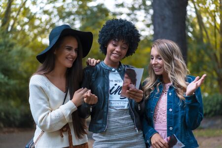 Lifestyle session. Three good friends in a park having fun, a blonde, a brunette and a Latin girl with afro hairの写真素材