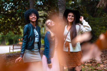 Lifestyle session. Three good friends in an autumn session under a tree with falling leaves, a blonde, a brunette and a Latin girl with afro hairの写真素材