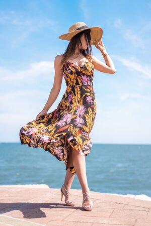 Street style, a young brunette in a beautiful flower dress moved by the wind and a hatの写真素材