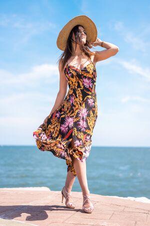 Street style, a young brunette in a beautiful flower dress moved by the windの写真素材