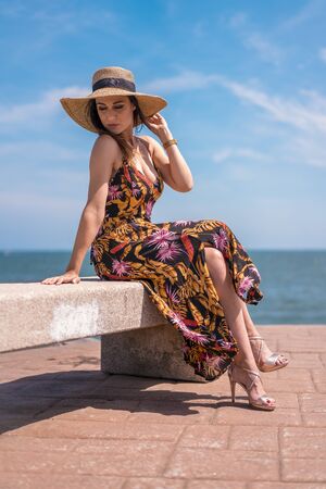 Lifestyle, a pretty young brunette in a floral dress and a straw hat by the seaの写真素材