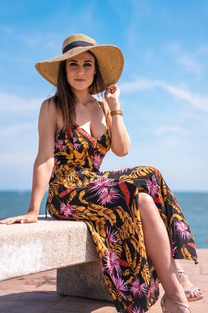 A young brunette woman in a dress and in a straw hat by the seaの写真素材