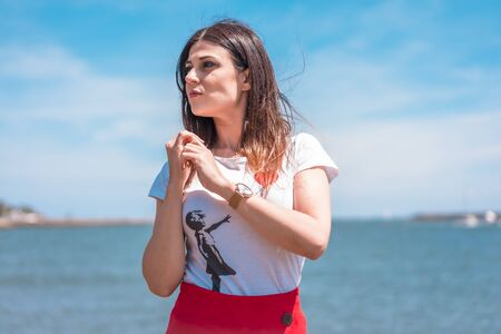 Street style, portrait of young brunette in white t-shirt on the coast with the sea in the backgroundの写真素材