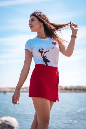 Street style, portrait of a pretty brunette in a white t-shirt and a short red skirtの写真素材