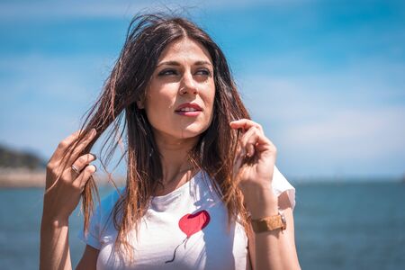 Lifestyle, a dreamy brunette looking left in a white t-shirt, a red short skirt by the seaの写真素材