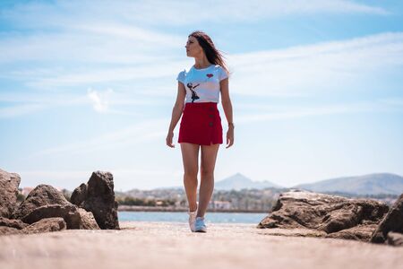 Street style, young brunette in white t-shirt walking along the promenade looking leftの写真素材