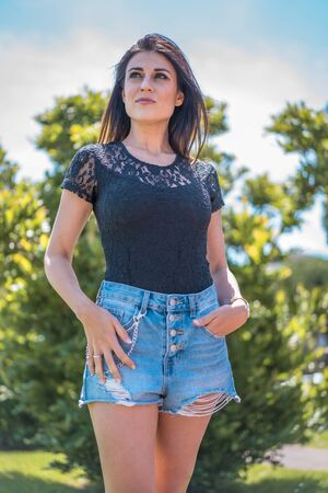 Lifestyle, portrait of a serious young brunette in a black t-shirt and denim shorts looking to the leftの写真素材