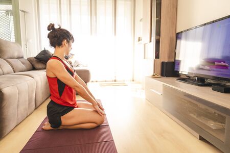 Yoga at home, a young woman sitting at home in the room with a nice light. In the coronavirus quarantineの写真素材