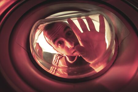 Is there life in this world? A young man looking out the window of a ship with a red light. Photo inside a washing machineの写真素材