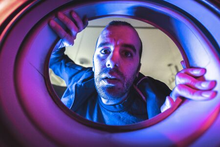 Portrait from inside a washing machine of a young caucasian man, with blue and red lights and in the darkの写真素材