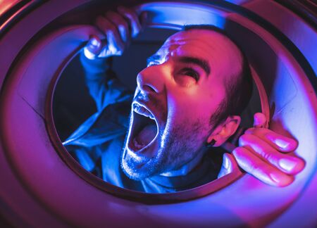 Portrait from inside a washing machine of a young caucasian man screaming, with blue and red lights and in the darkの写真素材