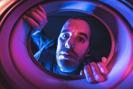 Portrait from inside a washing machine of a scared young Caucasian manの写真素材