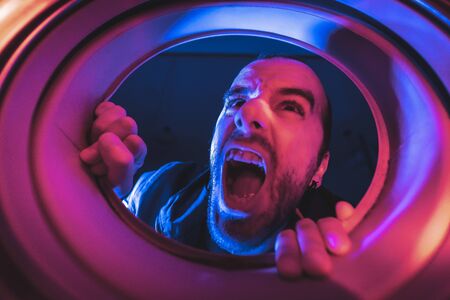 Portrait from inside a washing machine of a young Caucasian man who wants to escapeの写真素材