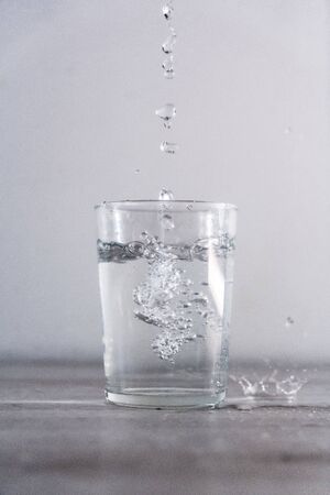 Throwing drops of water from above into a glass of water. Drink macro photographyの写真素材