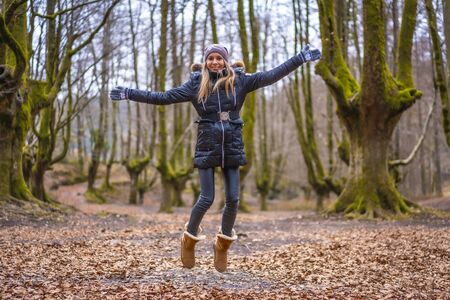 Lifestyle, a young blonde woman jumping for joy in a forest in autumnの写真素材