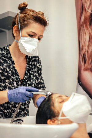 Hairdresser with security measures for the covid-19, new normality, social distance. Hairdresser washing hair to a client with mask