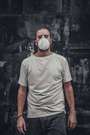A young man in a white shirt and mask at a black metal door. Health emergency, pandemic Covid-19の写真素材