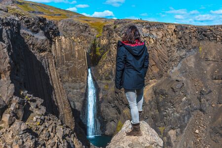 A young woman looking at the waterfall above Hengifoss from above. Icelandの写真素材