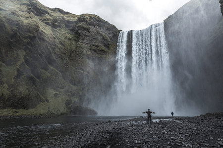 A tourist with open arms at the bottom of the Skogafoss waterfall in the golden circle of the south...