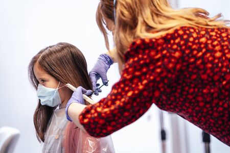 Hairdresser with mask and gloves cutting a girl's hair with scissors. Reopening with security measures for hairdressers in the Covid-19 pandemicの写真素材