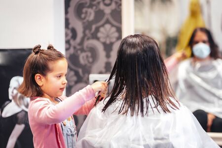 Client sitting by the mirror while waiting for her daughter to comb her hair. Reopening with security measures for hairdressers in the Covid-19 pandemicの写真素材