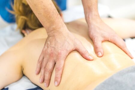 Physiotherapist doing a massage with two hands behind the back of a girl with a mask.の写真素材