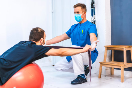 Physiotherapist with mask and a patient doing exercises. Physiotherapy with protective measures for...