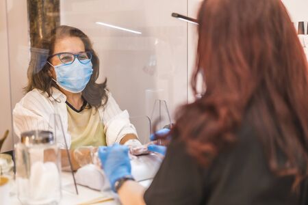 Beauty Salon, reopening of the business after the coronavirus pandemic. An employee with a face mask putting a cream on the client's hands. Covid-19の写真素材