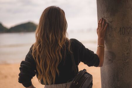 Lifestyle in the city with a blonde girl in white pants and a leather jacket near the beach. Apolllada in a column watching the seaの写真素材