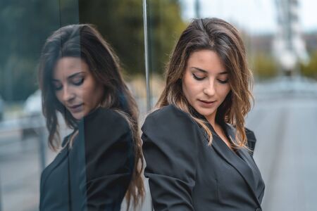 Street style, an enterprising young Caucasian woman entering the office to work in a black suit and heels. Reflected in the glass of the black glass building one spring morningの写真素材