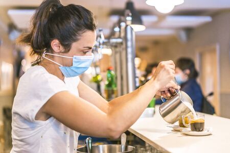 Photo session with a waitress with a face mask in a bar. New normality, security measures after the coronavirus pandemic, social distance, covid-19. Making a milk decafの写真素材