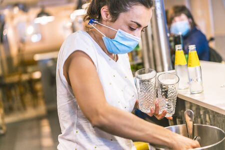 Photo session with a waitress with a face mask in a bar. New normality, security measures after the coronavirus pandemic, social distance, covid-19. Putting ice in a glassの写真素材