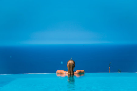 Summer lifestyle in an infinity pool with a young blonde Caucasian woman in a pink and purple bikini...