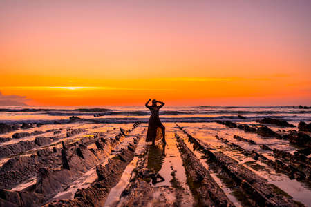 Lifestyle, a young brunette in a leather jacket and leopard dress on a sunset on the coast wearing sunglasses. Young man smoking and looking out to seaの写真素材