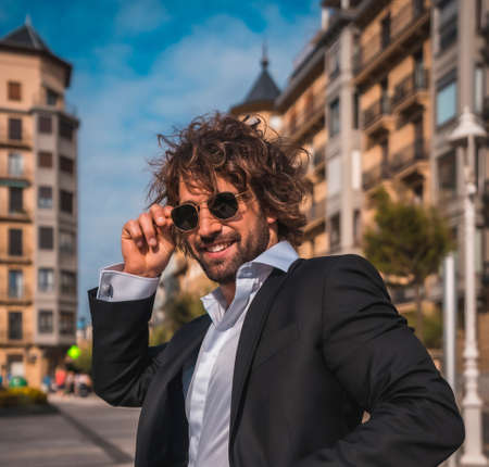 Street style an elegant black suit, white shirt and sunglasses. With a handsome young caucasian man with long hair in the city. Fashion editorial. Put your glasses onの写真素材